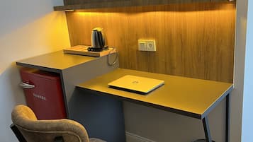 A compact workspace with a wooden accent wall, a desk with a laptop, a red cabinet, and a chair.
