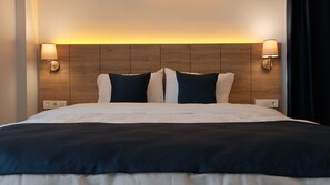 A hotel room with a wooden headboard, two bedside lamps, and a bed with white bedding and dark pillows. - The Blue Suites (Istanbul)