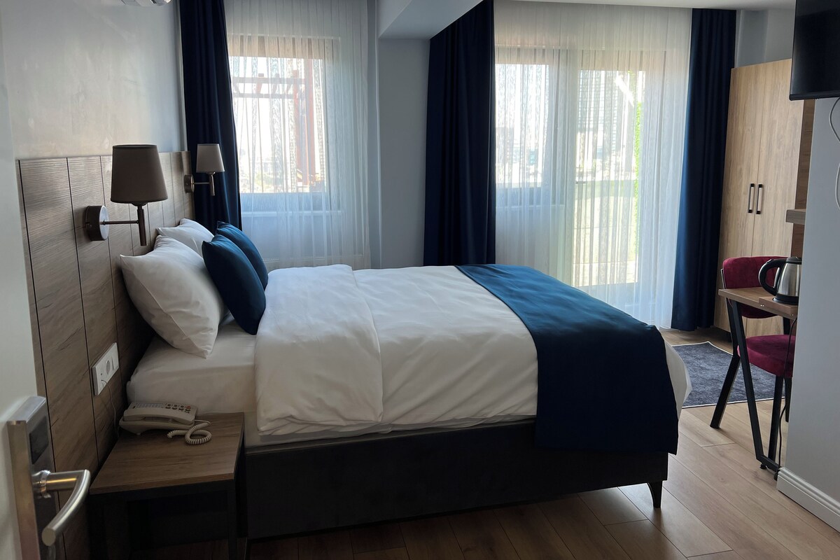 Habitación de hotel con cama, mesita de noche con teléfono, lámpara y televisor en la pared.