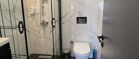 A modern bathroom with a glass-enclosed shower, a toilet, and a marble-tiled wall.