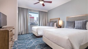 Habitación de hotel con dos camas, ventilador de techo, televisión y vista a la ciudad.