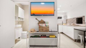 A modern kitchen with white cabinetry, a flat-screen TV mounted above the counter, and a small dining area with a white table and chairs. - Studio across the street from beach, top location (Playa Langosta)