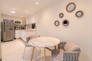Una cocina moderna con refrigerador, horno y microondas. Hay un comedor con una mesa redonda y sillas.