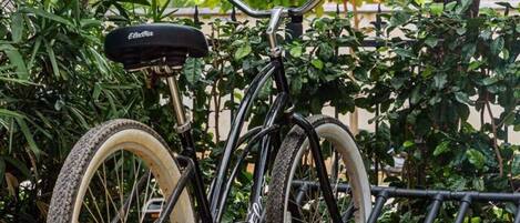 Una bicicleta asegurada a un soporte, con suelo de grava y follaje al fondo.