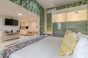 Un dormitorio moderno con una cama grande, un televisor, un escritorio y un baño con ducha de vidrio.