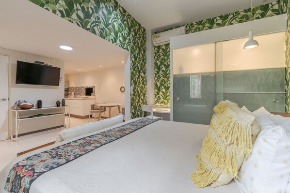 A modern bedroom with a large bed, a TV, a desk, and a bathroom with a glass shower. - Studio across the street from beach, top location (Playa Langosta)
