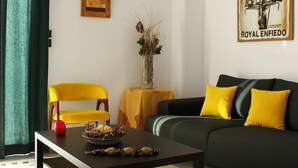 A living room with a black coffee table, a yellow armchair, a dark sofa with yellow cushions, a decorative vase, and a framed picture on the wall. - Central Old Town Stay - Bright & Fully Equipped (Patras)