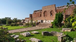 An ancient brick building with arched doorways and a surrounding garden with stone planters and greenery. - Central Old Town Stay - Bright & Fully Equipped (Patras)