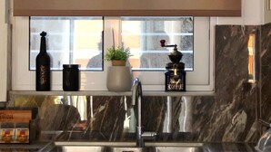 A kitchen with a window, a sink, cabinets, a coffee machine, and a bottle. - Central Old Town Stay - Bright & Fully Equipped (Patras)