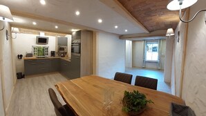 A modern kitchen with built-in appliances, a dining area with a wooden table and chairs, and a view of the adjacent living space.