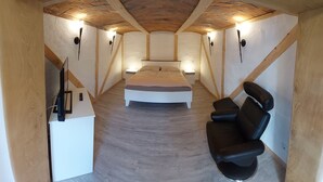 A bedroom with a bed, a black leather chair, and a desk with a computer.