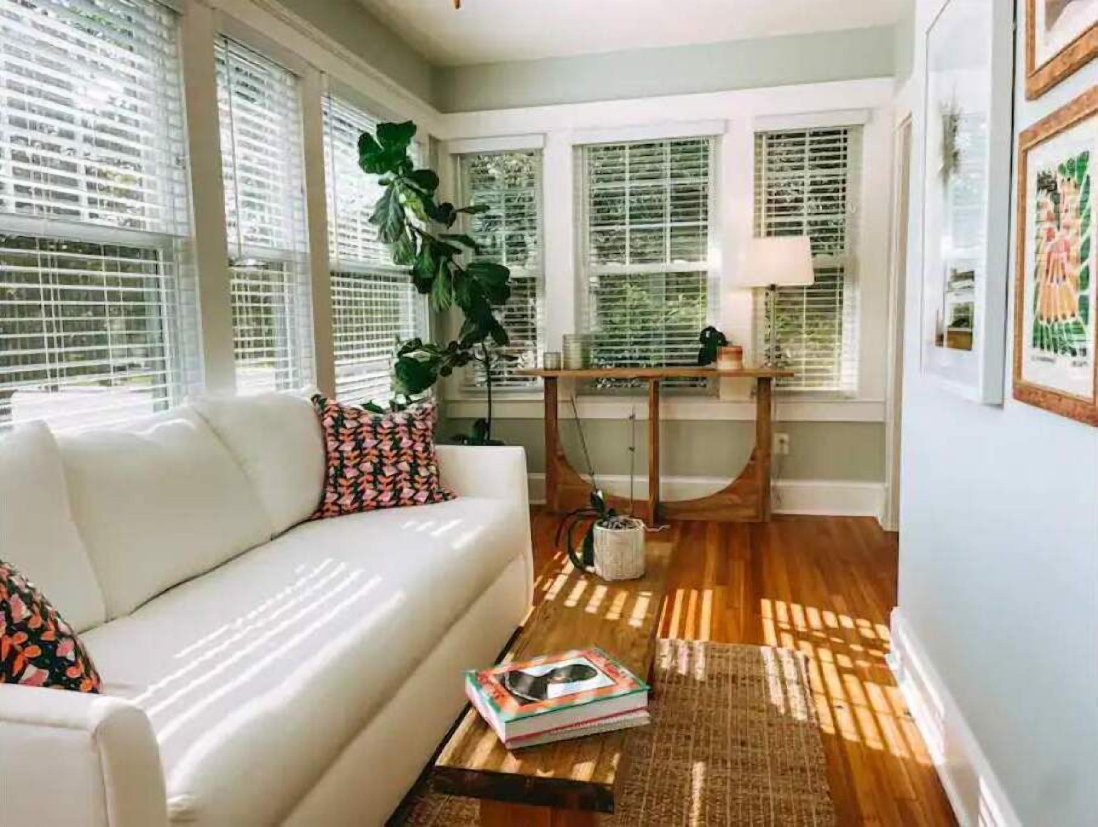 A well-lit room with a white sofa, a large plant, and a wooden coffee table with books.