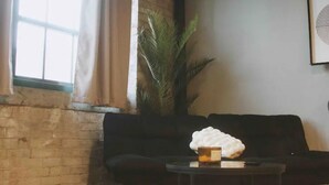 A room with a brick wall, a black sofa, a round table with a white object, and a large plant. - Premier Loft Downtown Detroit (Detroit)