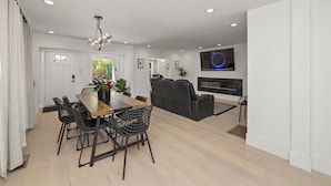 A modern living room with a wooden dining table, black chairs, a black sofa, a fireplace, and a mounted TV. - 2BR Home in Menlo Park Near Stanford University! (Menlo Park)