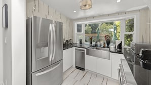 A modern kitchen with stainless steel appliances, white cabinetry, and a large window offering a view of greenery. - 2BR Home in Menlo Park Near Stanford University! (Menlo Park)