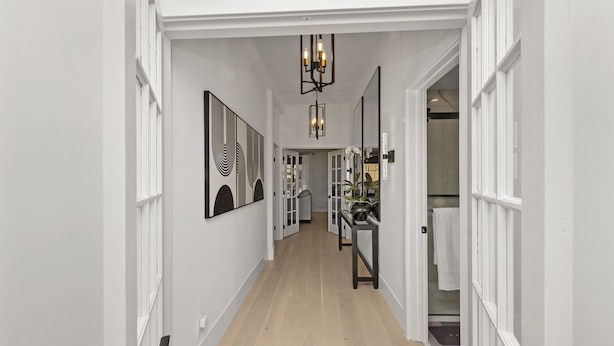 A hallway with white walls, wooden flooring, and a chandelier. There are framed artworks on the walls and a door leading to a bathroom. - 2BR Home in Menlo Park Near Stanford University! (Menlo Park)