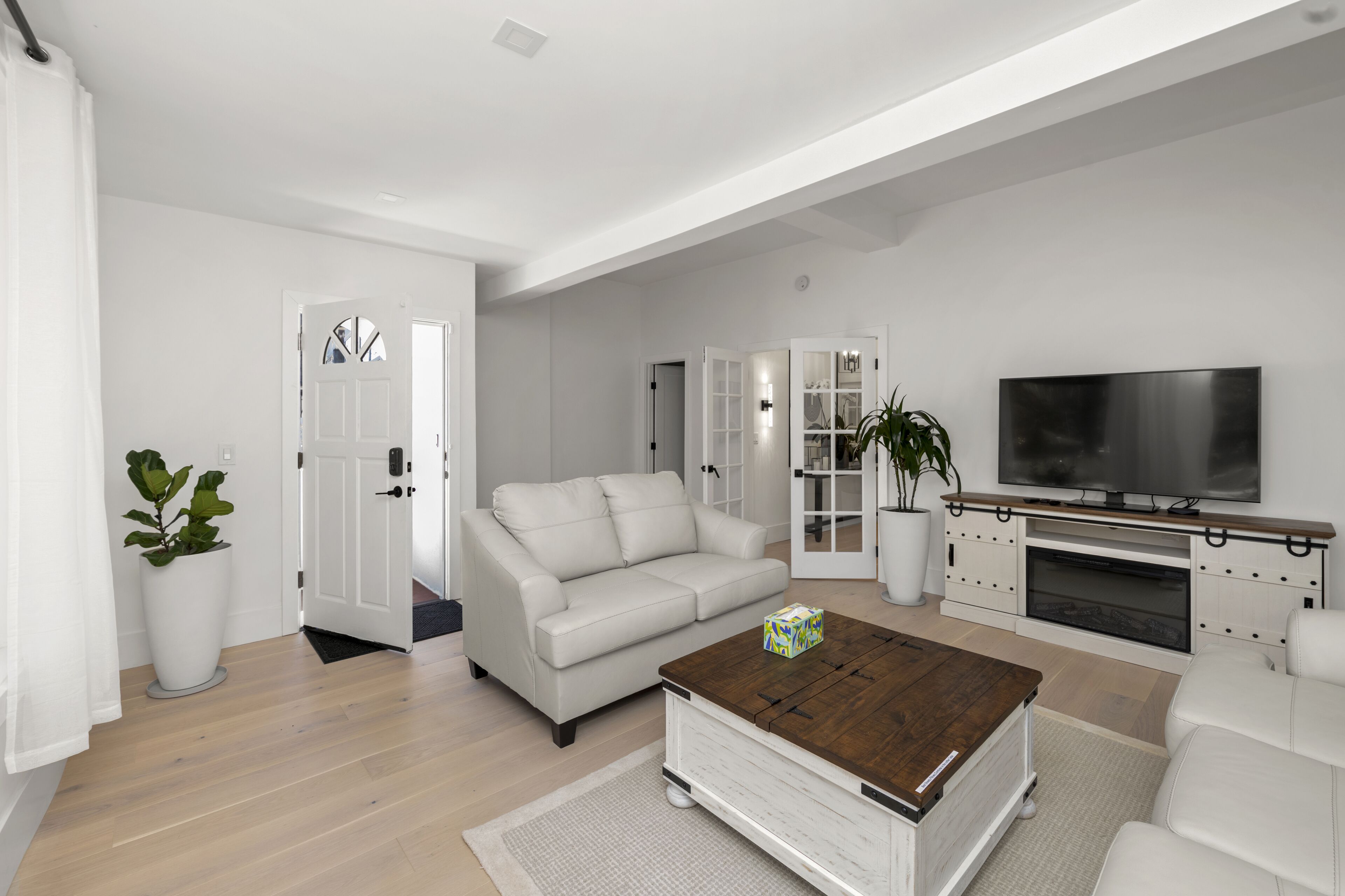 Un salon moderne avec un canapé blanc, une table basse en bois, un téléviseur à écran plat et une cheminée.