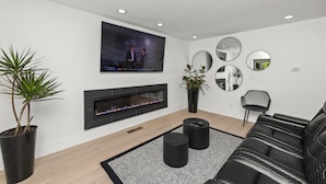 A modern living room with a flat-screen TV, a fireplace, black leather sofa, and decorative mirrors. - 2BR Home in Menlo Park Near Stanford University! (Menlo Park)