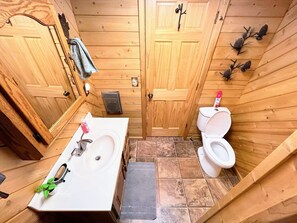 Et lille badeværelse i træ med vask, toilet og to døre.