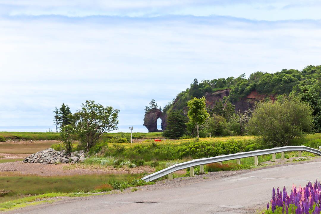 Un paysage rural avec une route, un pont métallique et une formation rocheuse naturelle en arrière-plan.