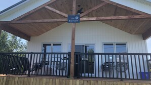 Een kusthuis genaamd "The Bayview" met een houten terras, zwarte balustrade en een overdekte patio.