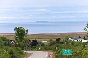 Une route côtière, un panneau indiquant la limite du village, un bâtiment blanc et une vue sur la mer.