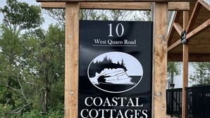 Houten bordje voor Coastal Cottages, gelegen aan 10 West Quaco Road, St. Martins, N.B., met een QR-code voor reserveringen.