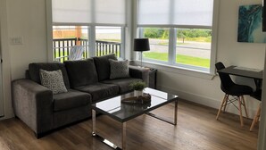 Een moderne woonkamer met een grijze bank, een glazen salontafel en een eethoek met een zwarte stoel en tafel.