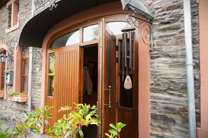Un edificio de piedra con puerta de madera, una campana colgante y ventana con vistas.