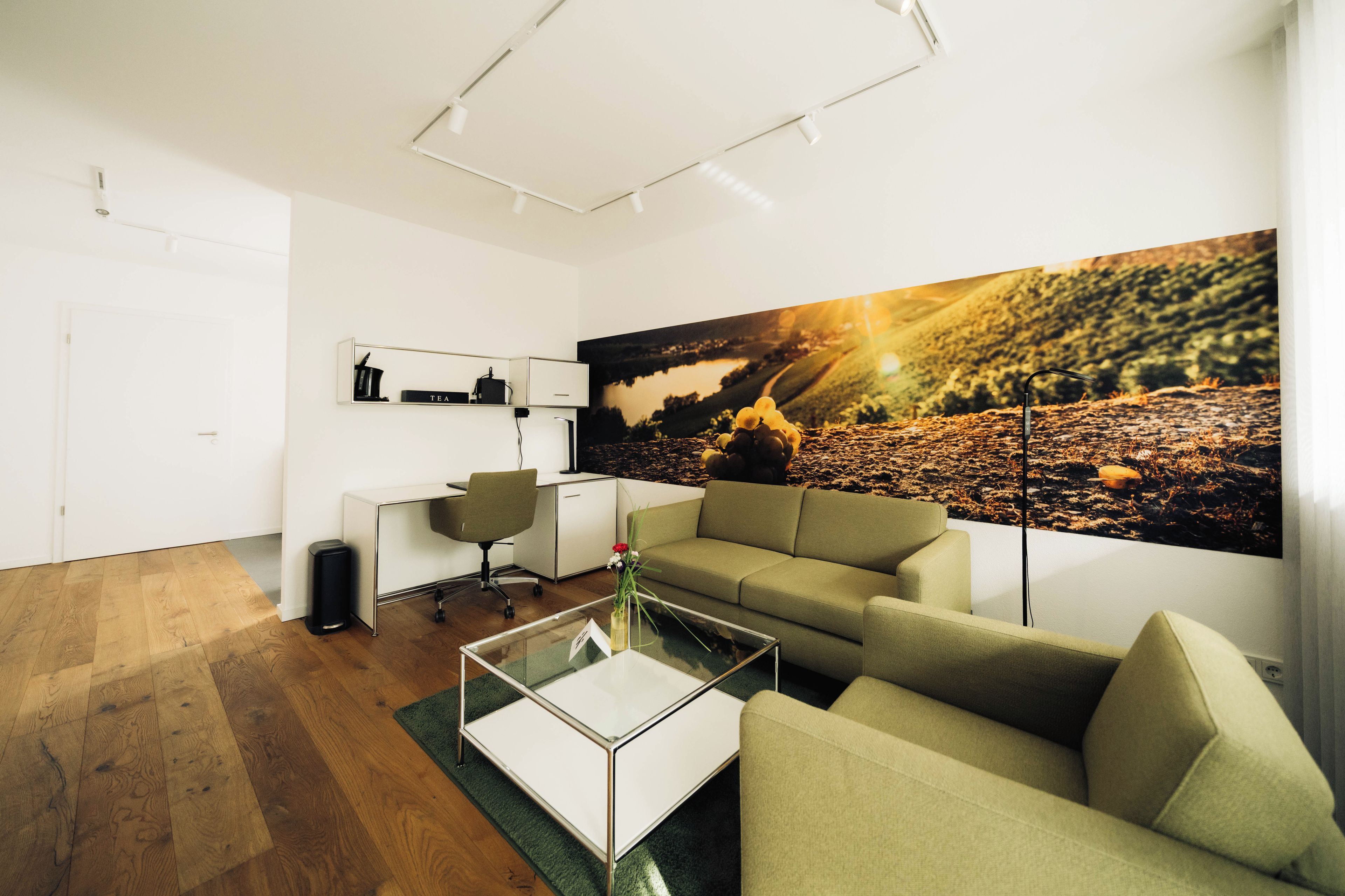 A modern office space with a desk, chair, sofa, and a large landscape painting.