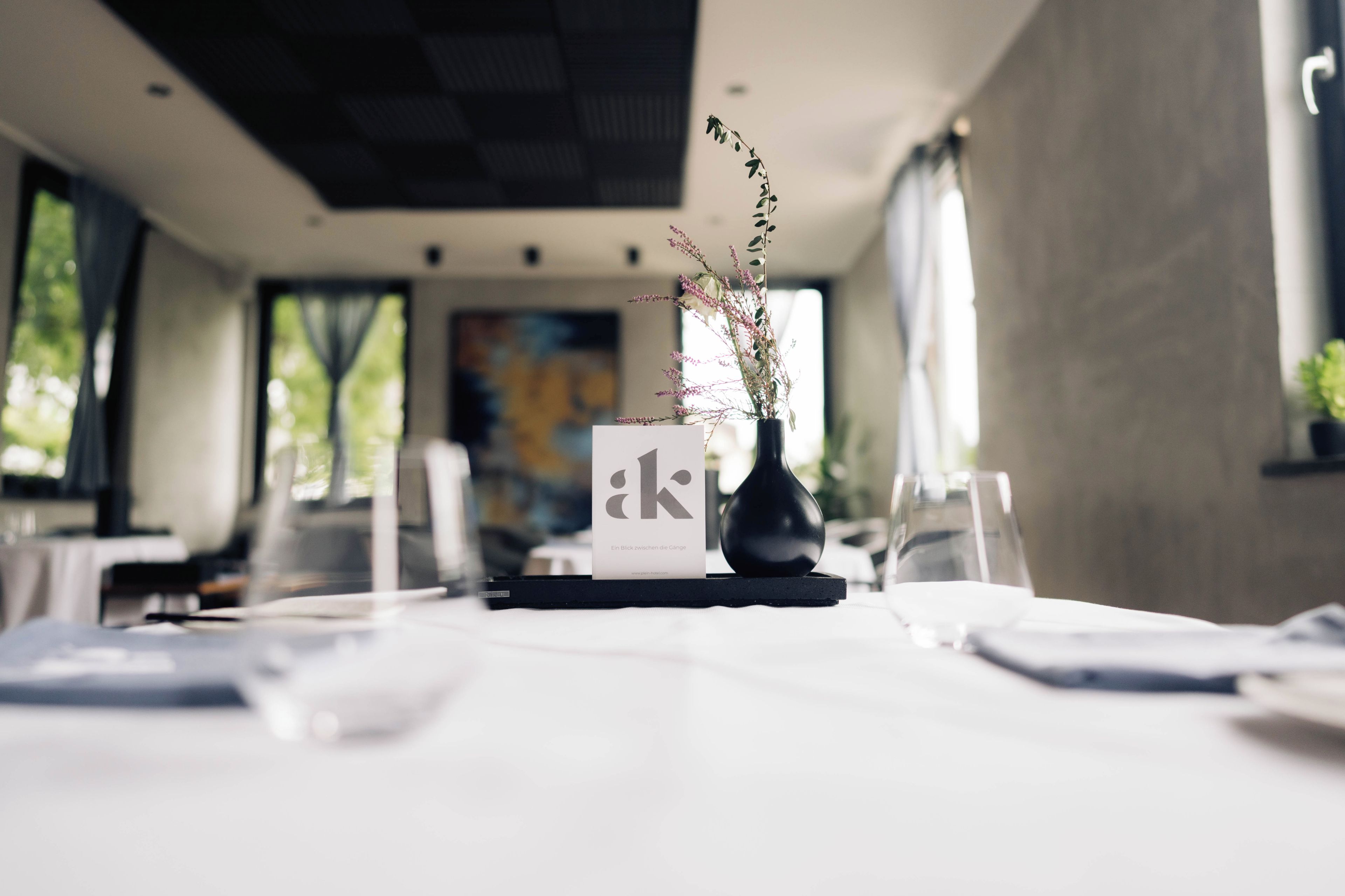 Une salle à manger d’hôtel avec des tables dressées pour les clients, un vase rempli de fleurs et un présentoir à menus.