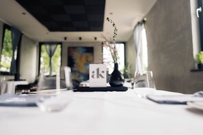Un comedor de hotel con mesas dispuestas para los huéspedes, un jarrón con flores y un atril para el menú.