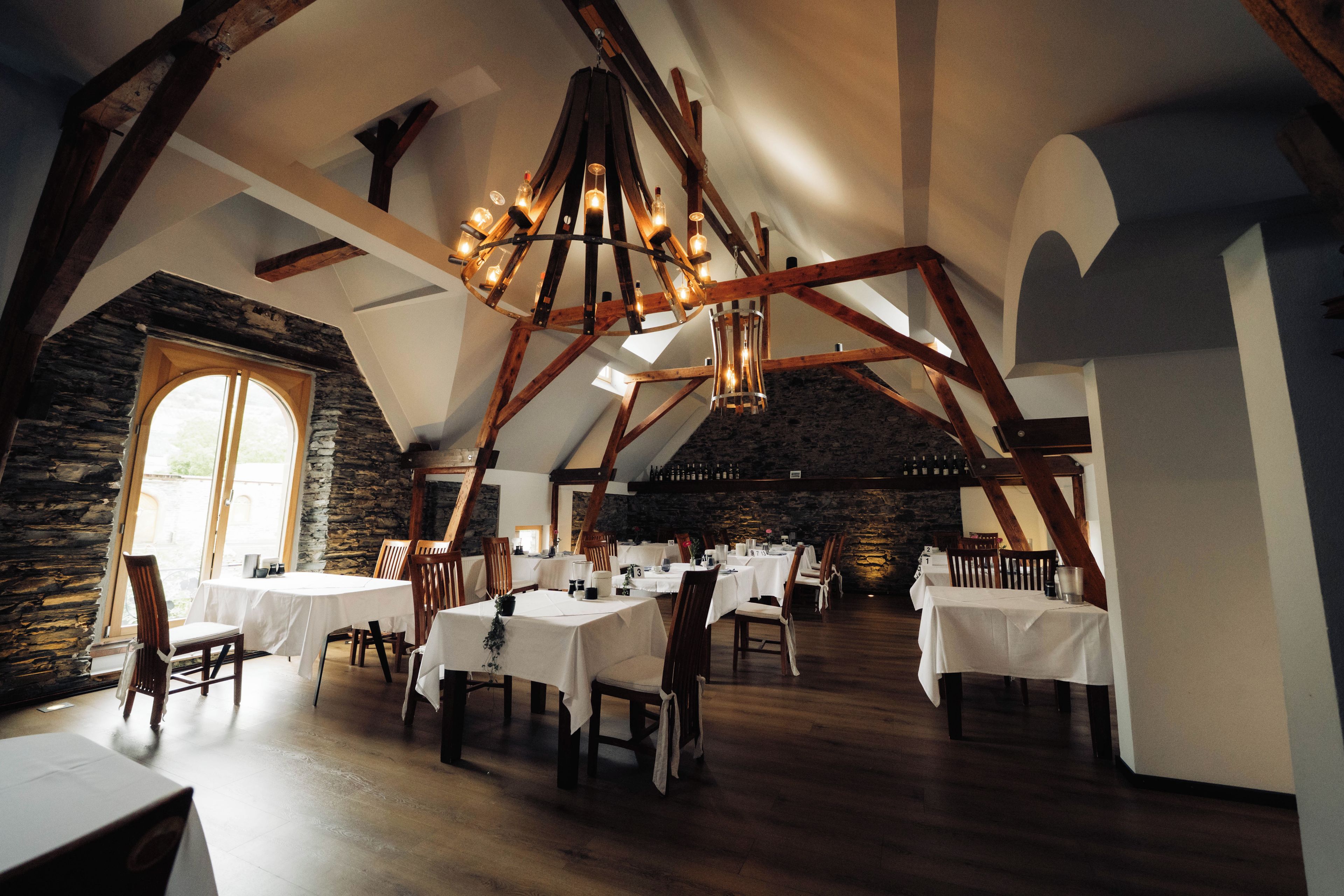 A restaurant with high wooden beams, stone walls, and multiple tables set for dining.