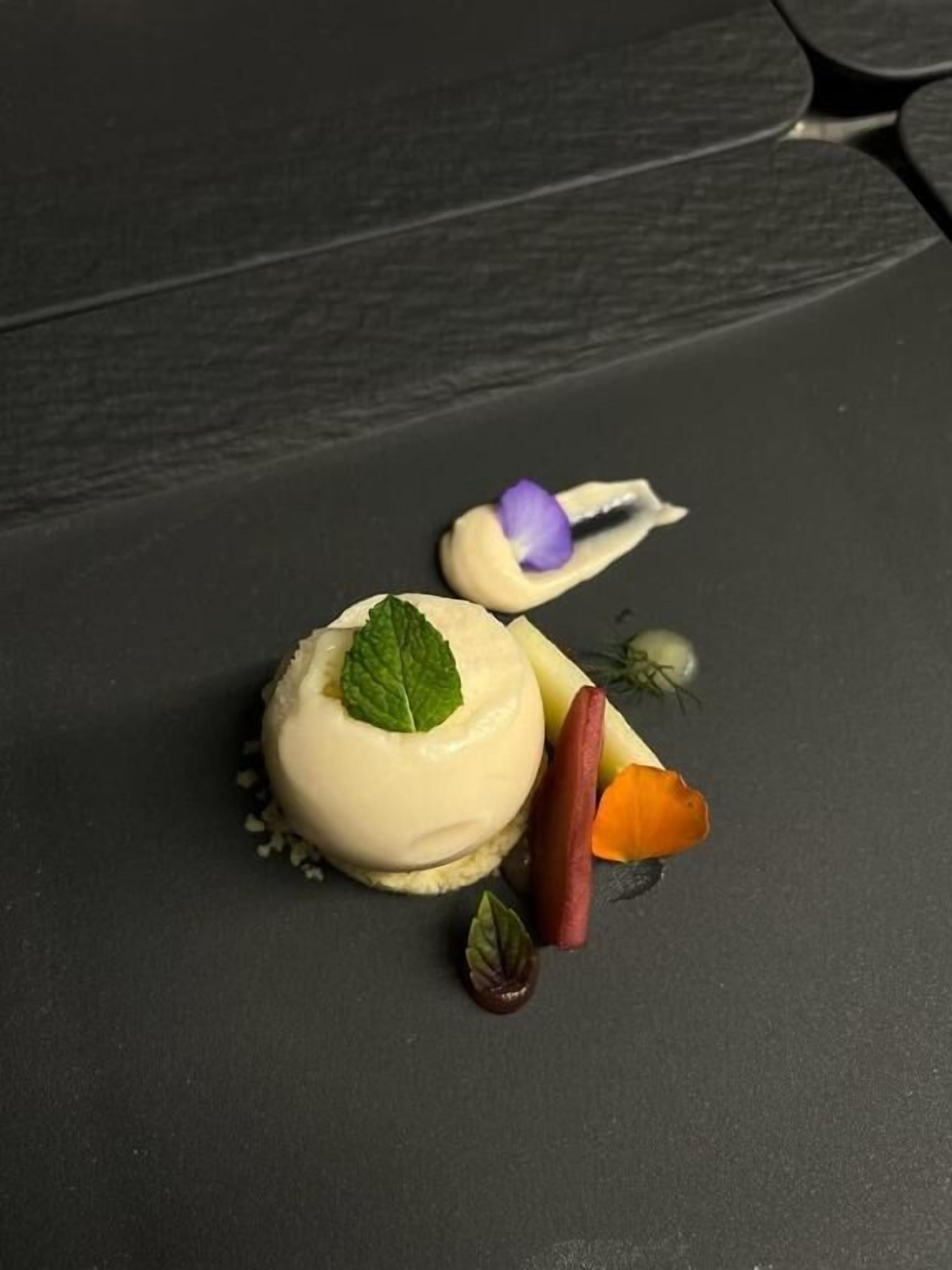 A dessert on a dark slate plate with a mint leaf garnish.