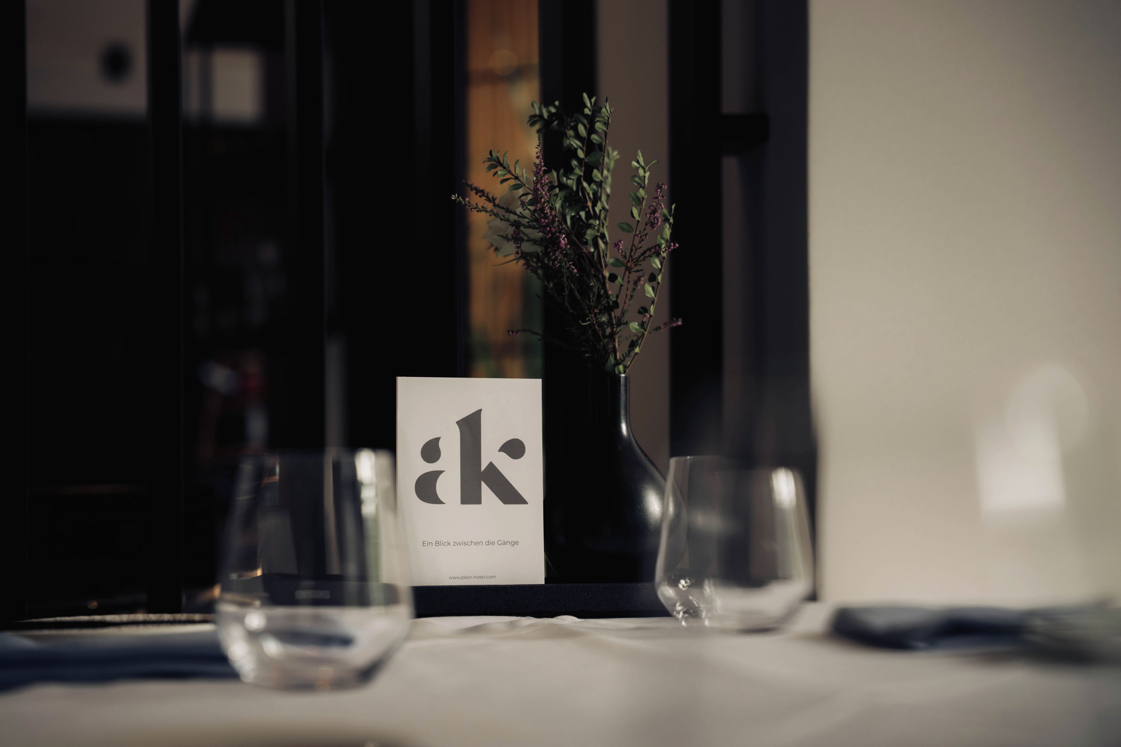 Une table avec un vase de fleurs, un menu et deux verres.