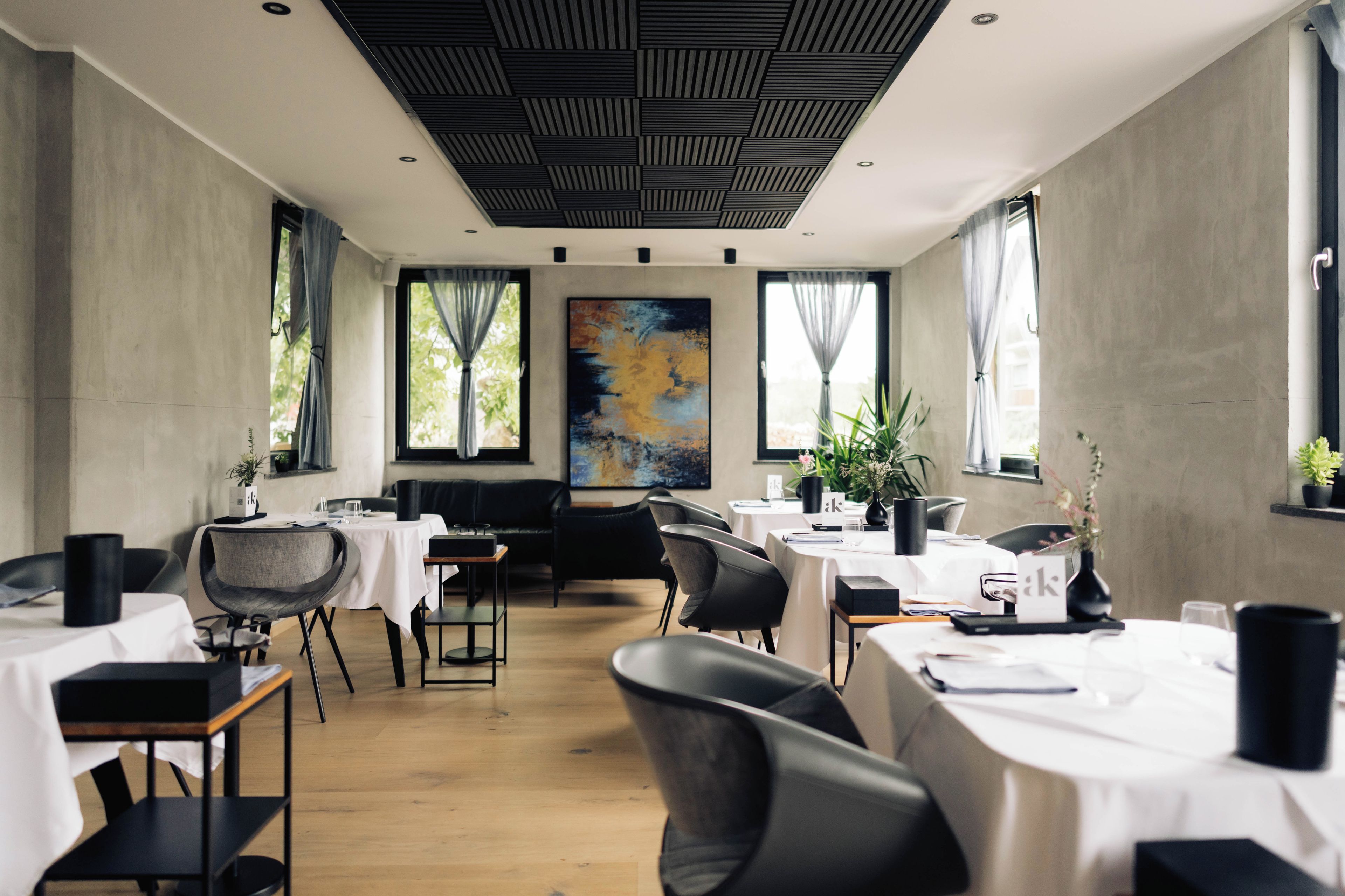 Une salle à manger moderne, avec des tables, des chaises et un grand tableau abstrait.