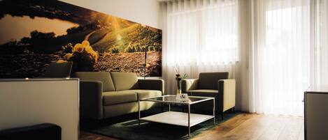 A modern living room with a sofa, armchairs, a coffee table, and a large painting.
