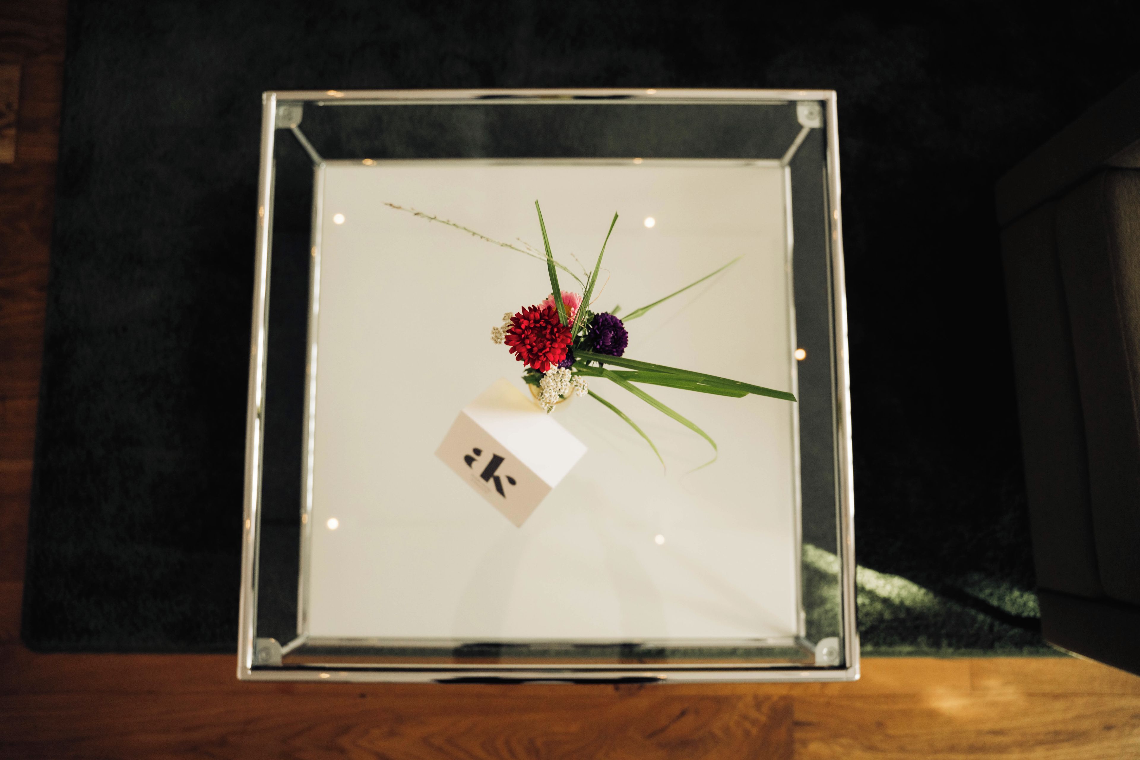 A framed floral arrangement with a card labeled 'K' inside a clear display case.