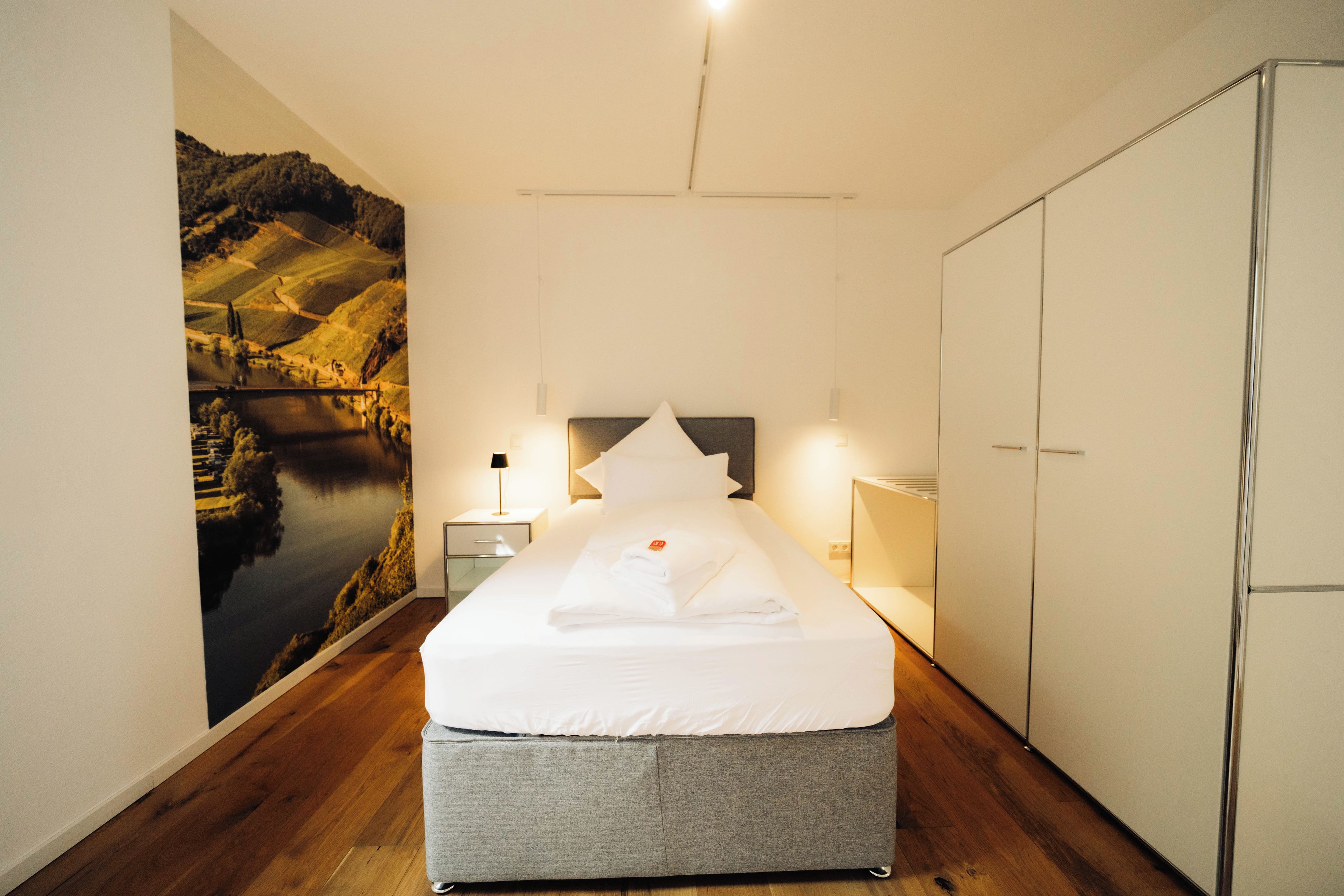 A bedroom with a bed, nightstand, lamp, wardrobe, and a large wall mural.