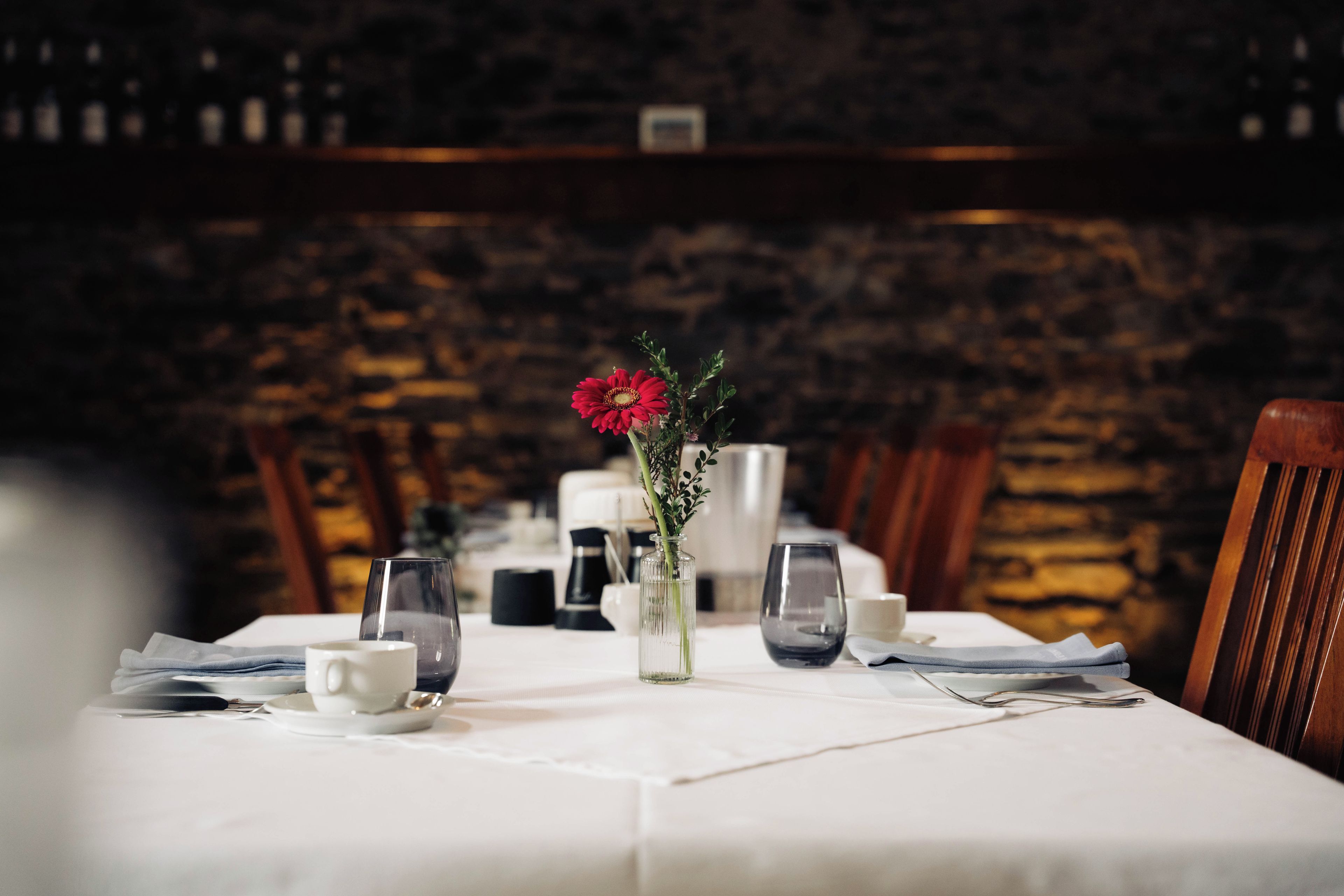 Una mesa puesta con un jarrón de flores, vasos y cubiertos.