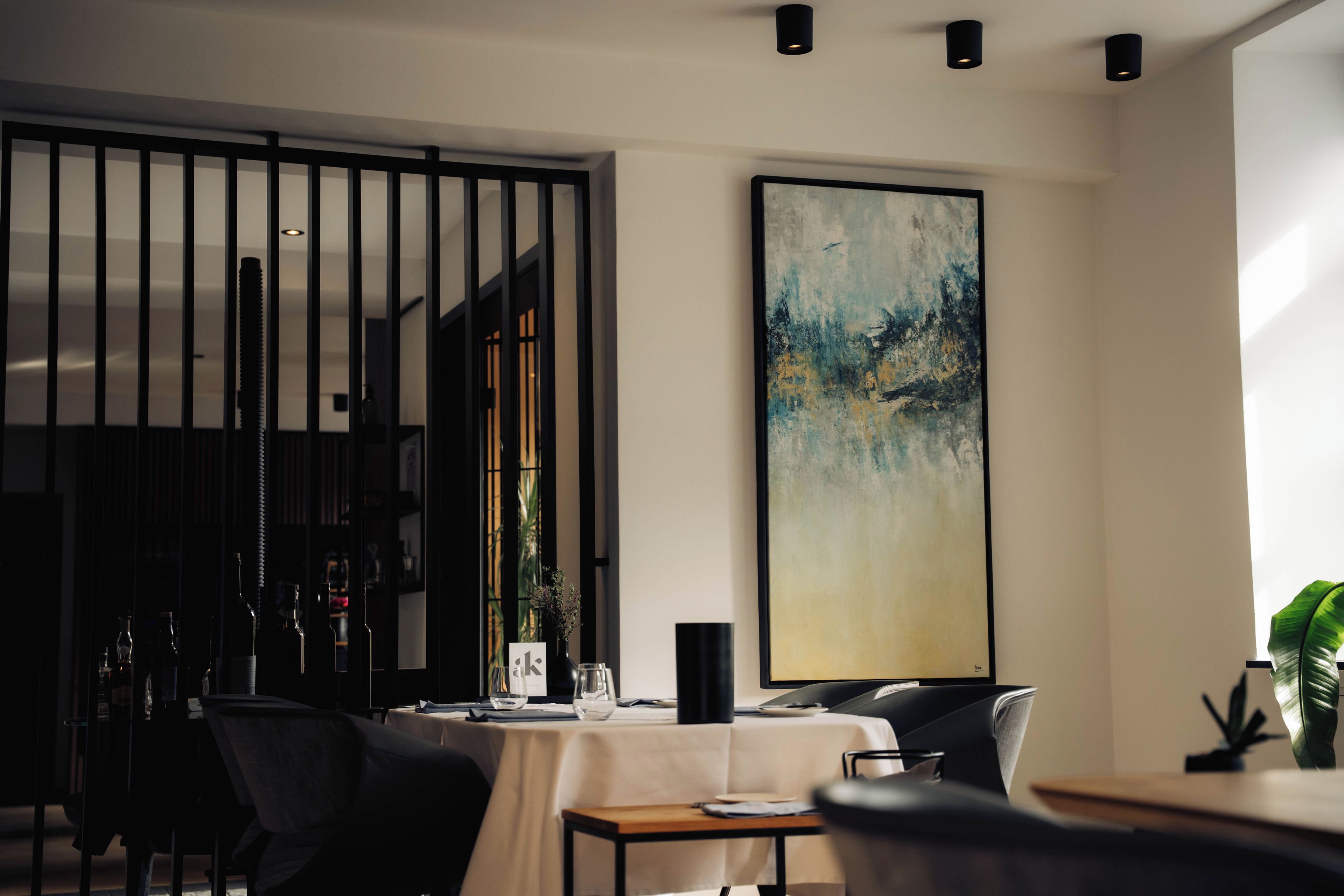 Un comedor moderno con una mesa dispuesta para dos personas, un cuadro abstracto grande en la pared y una planta decorativa.