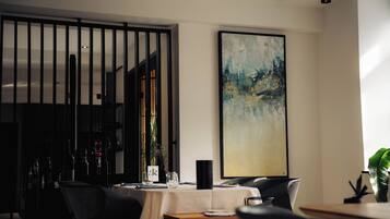 Un comedor moderno con una mesa dispuesta para dos personas, un cuadro abstracto grande en la pared y una planta decorativa.