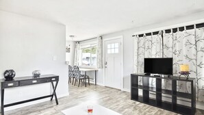 Una sala moderna con televisor, un comedor con sillas y una mesa blanca con vasos.