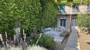 A stone pathway leading to a white metal bench and table set against a wall covered in green ivy. - Les Glycines (Trausse)