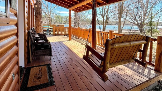 A wooden deck with a swing chair, a bench, and a row of wicker chairs.