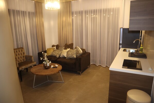 A modern living room with a sofa, a coffee table, and a dining area with a sink and a mirror.
