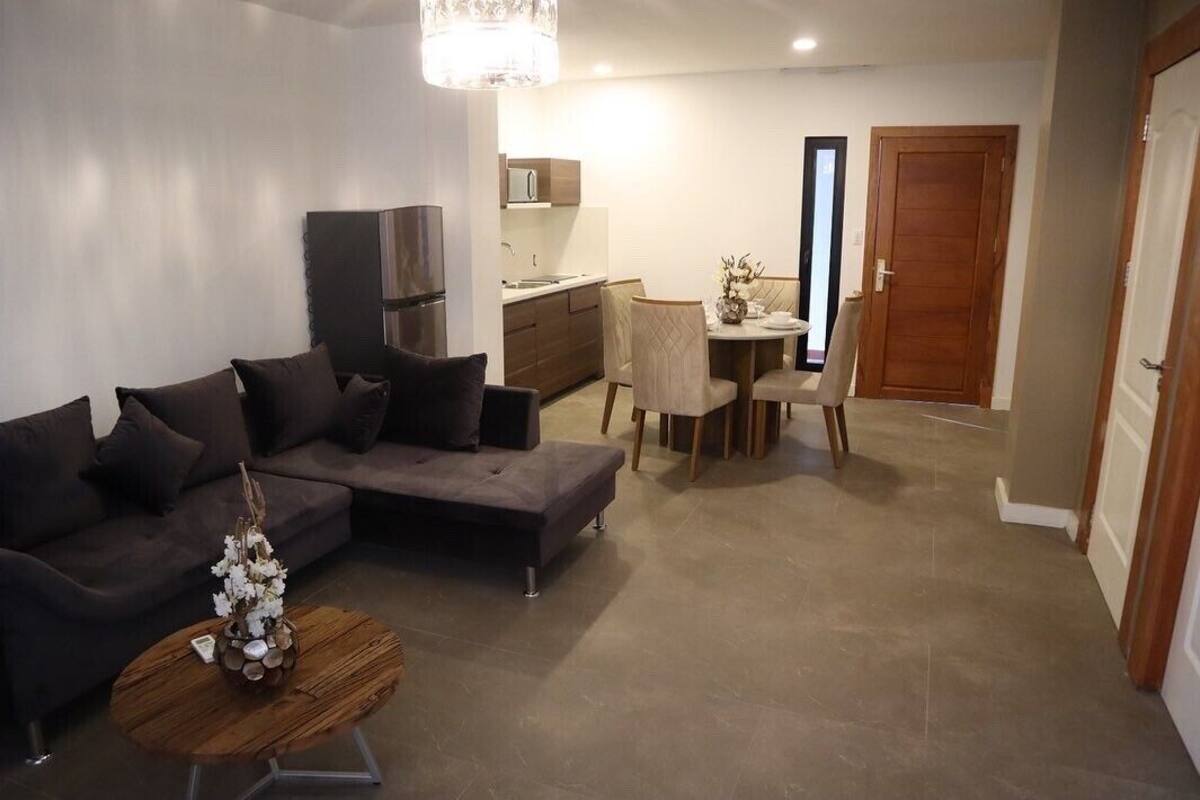 A modern living room with a dark grey sofa, a wooden coffee table with a vase, and a dining area with a table and chairs.