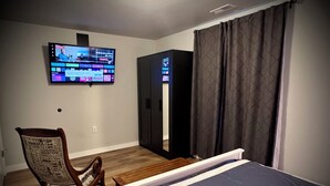Ein Hotelzimmer mit Bett, Wandfernseher, Holzstuhl und Kleiderschrank.