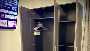 Ein begehbarer Kleiderschrank mit Kleiderstange, einer Tür mit Sicherheitshinweis und einem Fernseher, der einen Nachrichtensender zeigt.