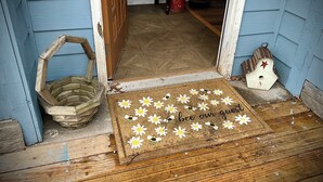 Eine Holztür mit Fußmatte, verziert mit Margeriten und Bienen, und dem Schriftzug "bee our guests".